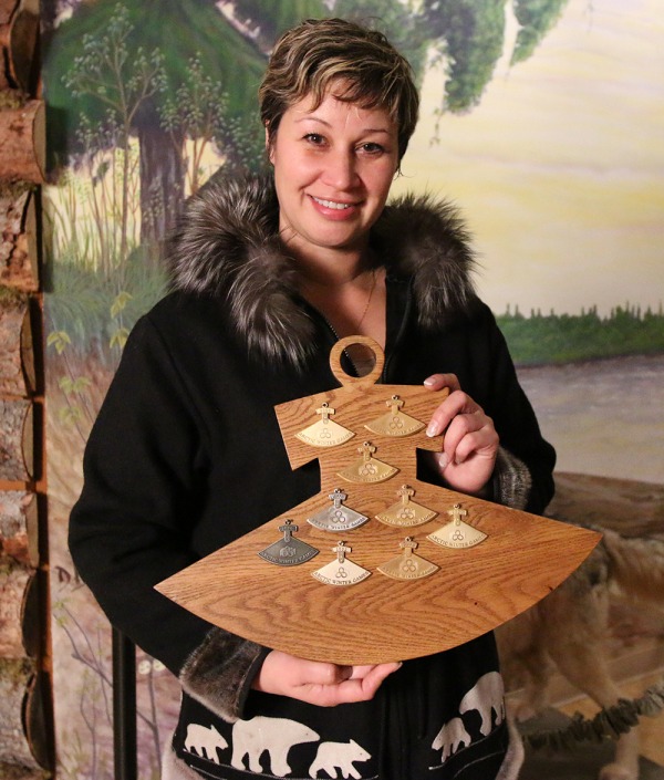 Meika McDonald holding wooden ulu shaped board with her ulu's mounted on the board