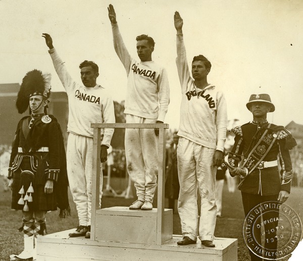 Photograph of three athletes standing on podium, Percy Williams in centre