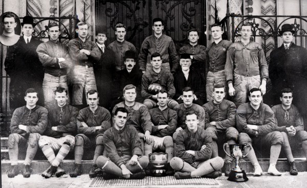 Photograph men in football uniform with two trophies