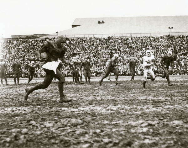photograph of a player running with football through muddy field