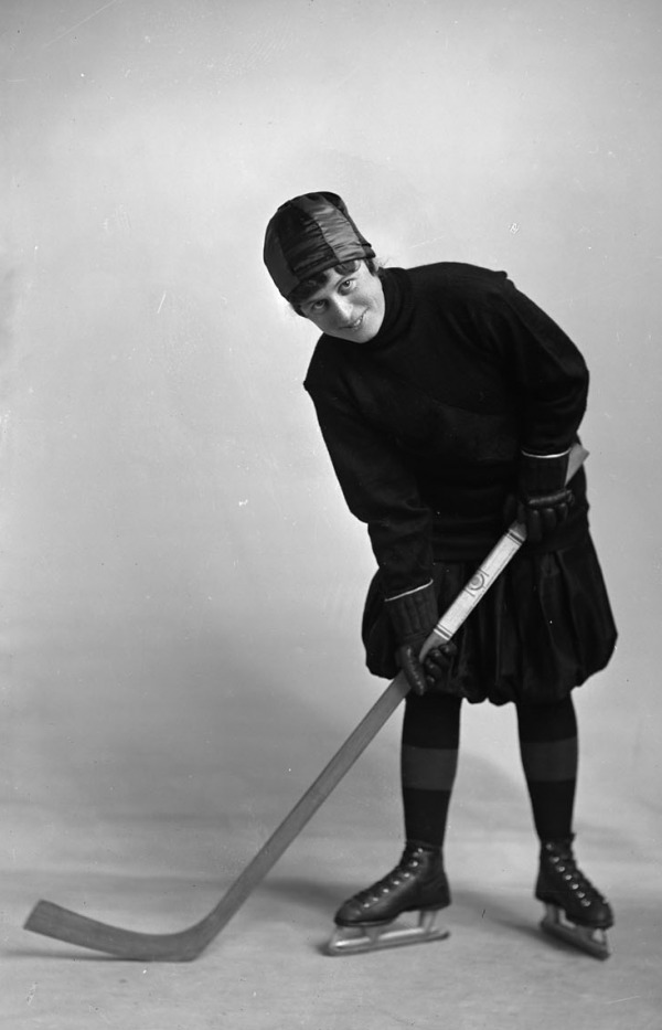 photograph of woman wearing bloomers on ice skates holding hockey stick